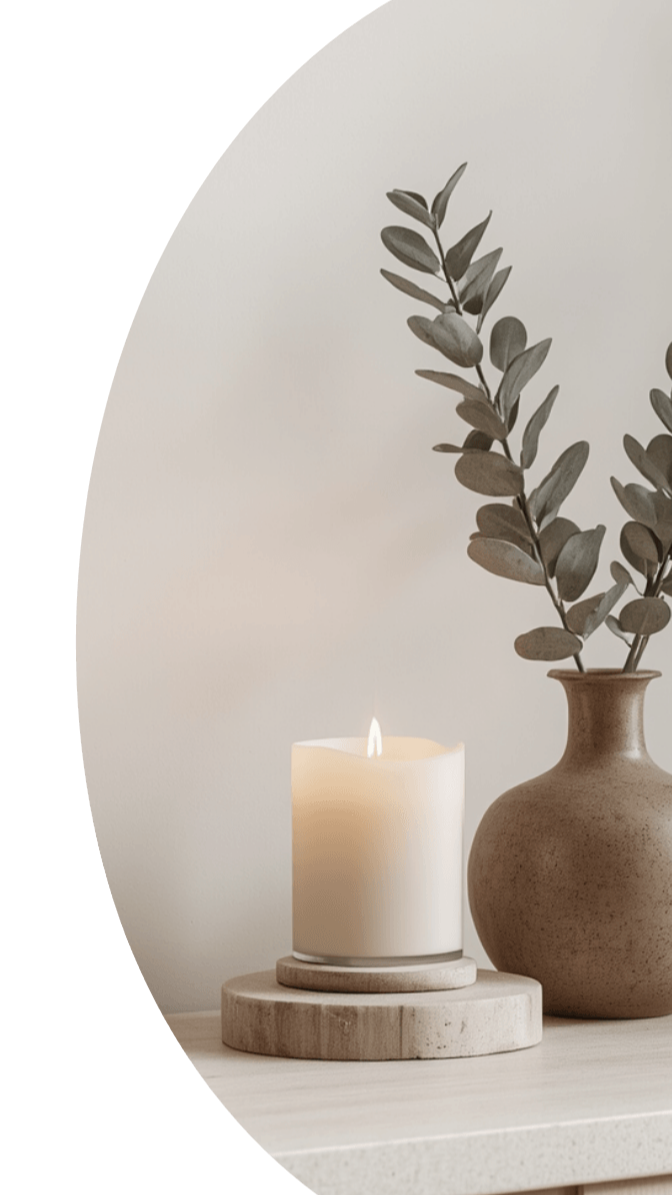 A calm image of a candle next to a vase with dried eucalyptus